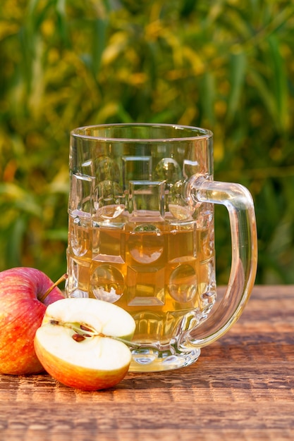 Copa de cristal de sidra de manzana y manzanas sobre tablas de madera con hojas de un árbol en el fondo.