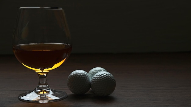 COPA DE LICOR CON PELOTAS DE GOLF SOBRE MESA DE MADERA RÚSTICA