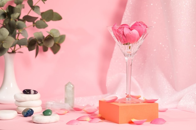 Copa de martini con piedras de flores y pétalos sobre fondo de color rosa