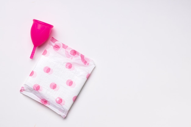 Copa menstrual y almohadilla higiénica sobre papel