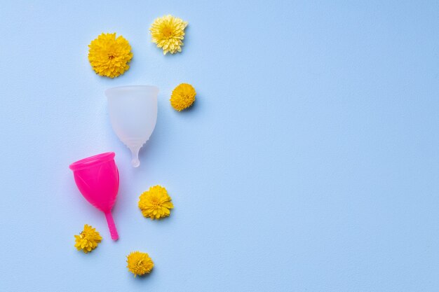 Copa menstrual con flores sobre fondo azul.