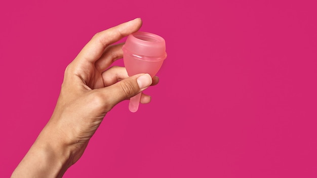 Foto copa menstrual higiénica de silicona rosa en mano femenina sobre fondo rosa