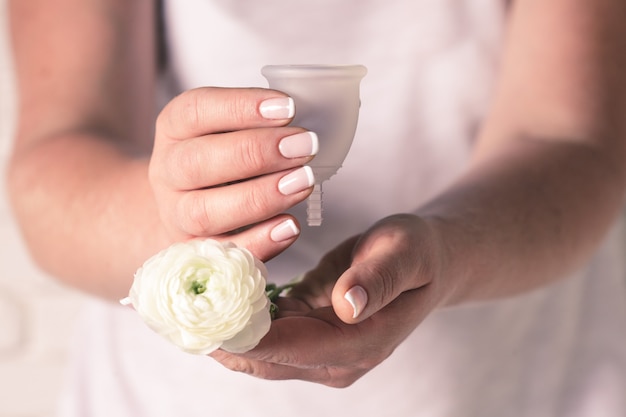 Copa menstrual en manos femeninas. Mujer sostiene taza higiénica de silicona y flores, nuevo dispositivo para minimizar el desperdicio y preservar el medio ambiente