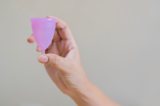 Copa menstrual de silicona reutilizable rosa en la mano de la mujer aislada sobre un fondo beige claro