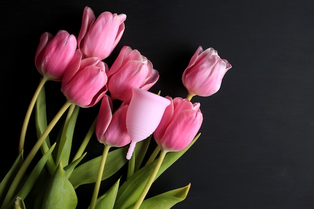 Copa menstrual y tulipanes rosas sobre fondo negro. La salud de la mujer.