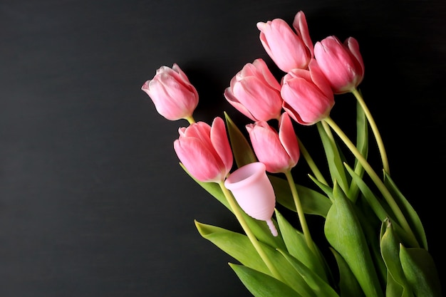 Copa menstrual y tulipanes rosas sobre fondo negro. La salud de la mujer.