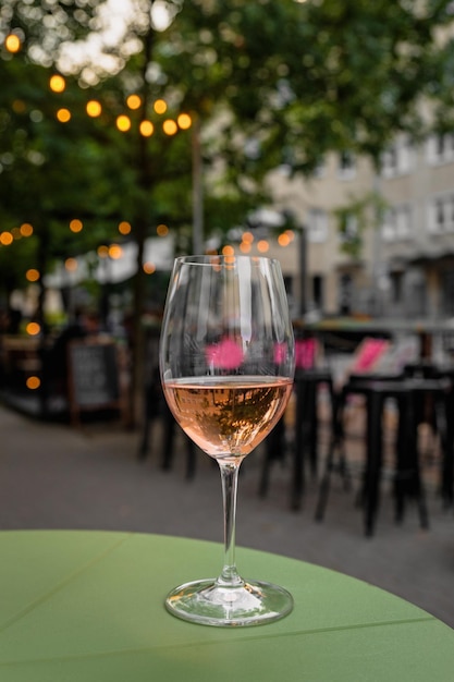 Una copa de refrescante vino rosado en la mesa verde de una terraza de café de la ciudad durante la cálida noche de verano en la calle de bokeh