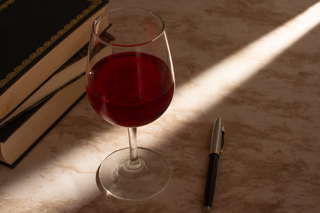 Foto copa de vino acompañada de unos libros con la luz de venta entrando por el lateral