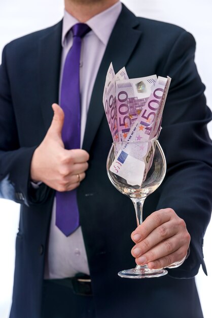 Copa de vino con billetes en euros en manos masculinas