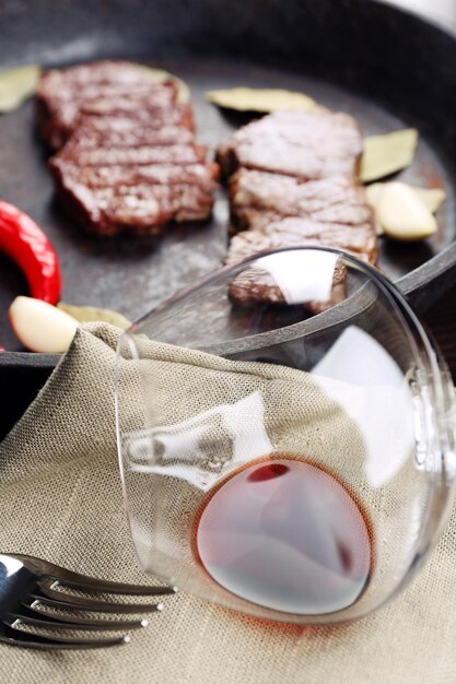 Foto copa de vino y bistec en sartén en la mesa de cerca