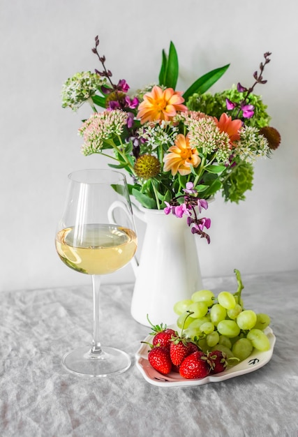 Copa de vino blanco fresas uvas un ramo de flores en una jarra blanca sobre la mesa en la habitación Delicioso aperitivo