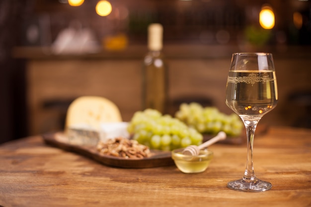 Copa de vino blanco con queso francés super consistente junto a nueces sobre mesa de madera rústica. Degustacion de comida. Uvas frescas.