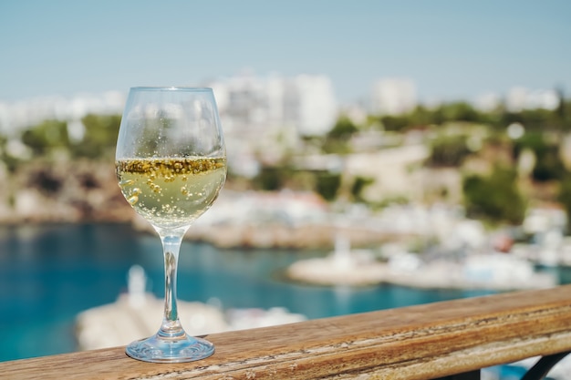 Copa de vino blanco con el telón de fondo del mar mediterráneo y el puerto con yates en un tour ...