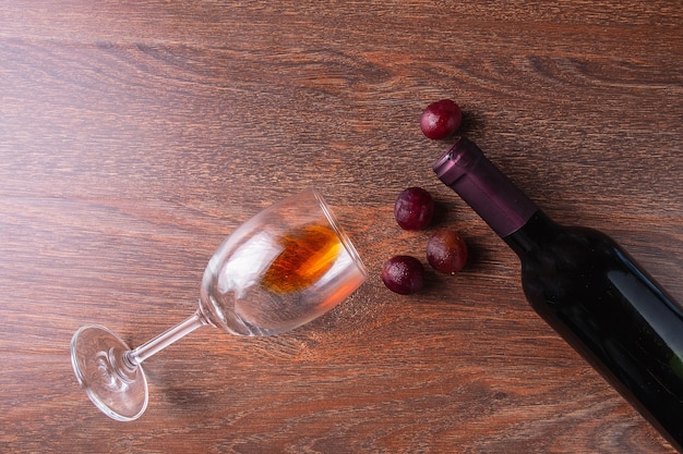 Copa de vino y botella de vino con uvas rojas sobre fondo de madera