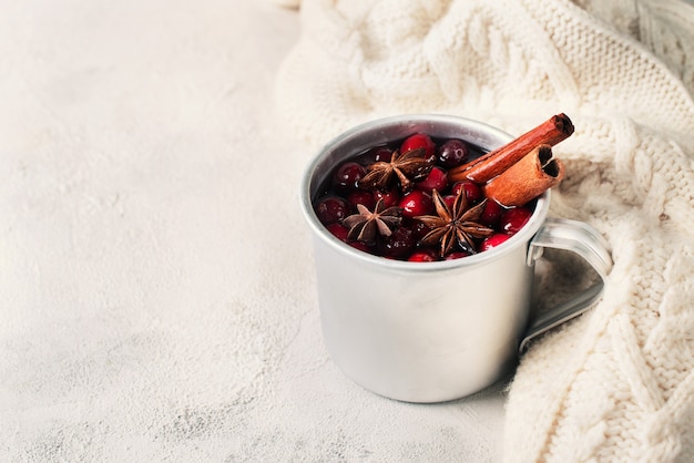 En copa de vino caliente con arándanos y especias sobre fondo de suéter blanco