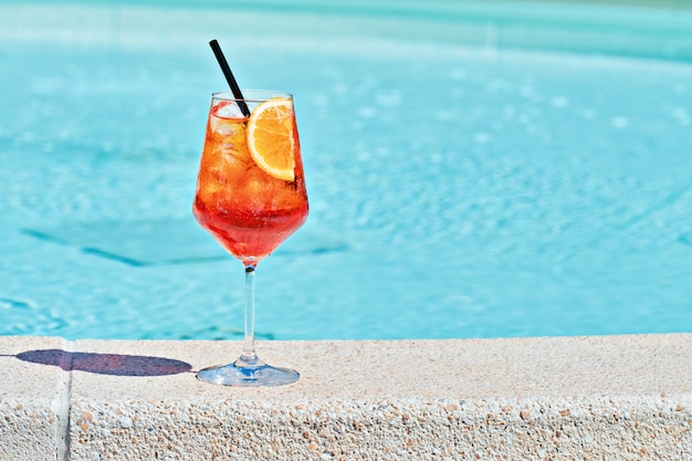 Copa de vino de cóctel frío Aperol spritz contra el agua turquesa de la piscina