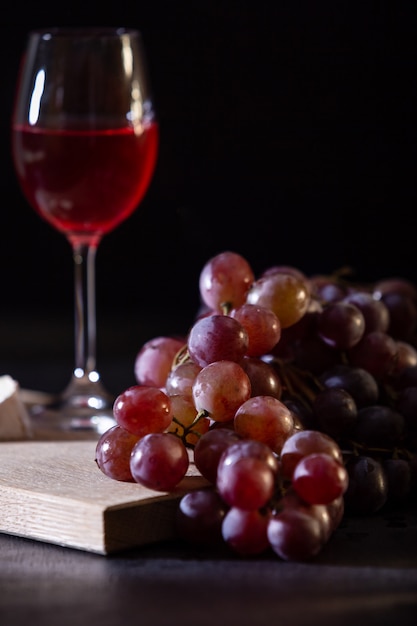 Copa de vino de frutas rojas. Primer de la vid de uva en un fondo oscuro en clave baja. Copia espacio