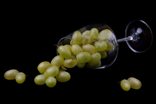 Una copa de vino llena de uvas verdes se encuentra sobre un fondo negro.