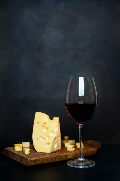 Copa de vino y sabroso queso en una tabla de cortar, piedra de fondo