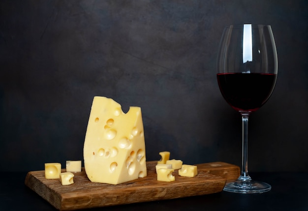 Copa de vino y sabroso queso en una tabla de cortar, piedra de fondo