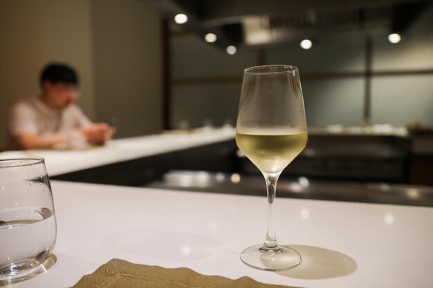 Una copa de vino se sienta en una mesa frente a un hombre con una camisa blanca.