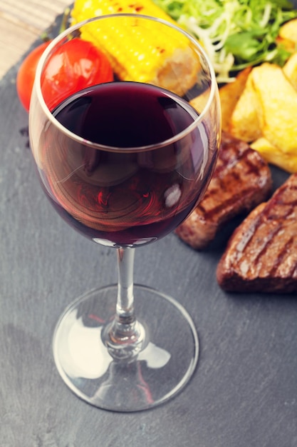 Foto copa de vino tinto y bistec con ensalada de papas a la parrilla