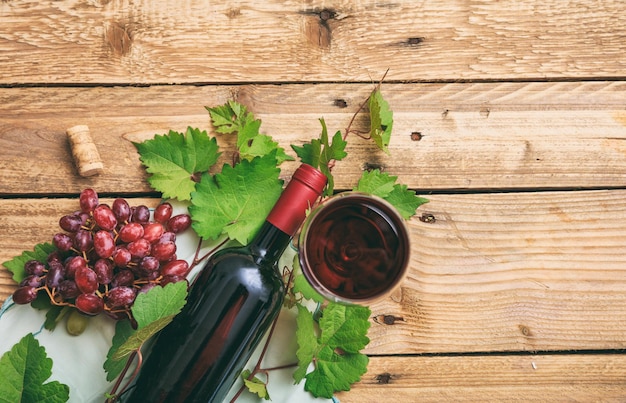 Copa de vino tinto y botella y uvas frescas en el espacio de copia de fondo de madera
