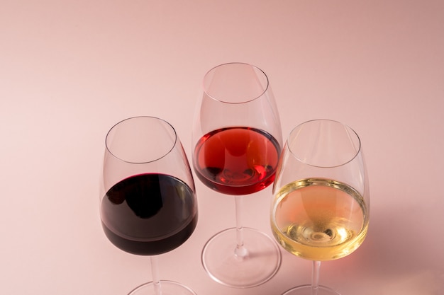 Copa de vino tinto y copa de vino rosado y copa de vino blanco sobre fondo rosa.