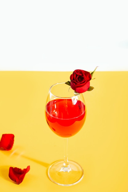 Copa de vino tinto decorada con capullos de rosas rojas y pétalos en el fondo amarillo