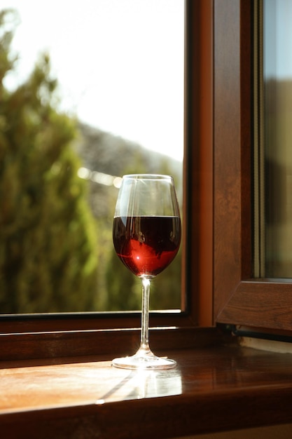 Copa de vino tinto se encuentra en el alféizar de la ventana de madera