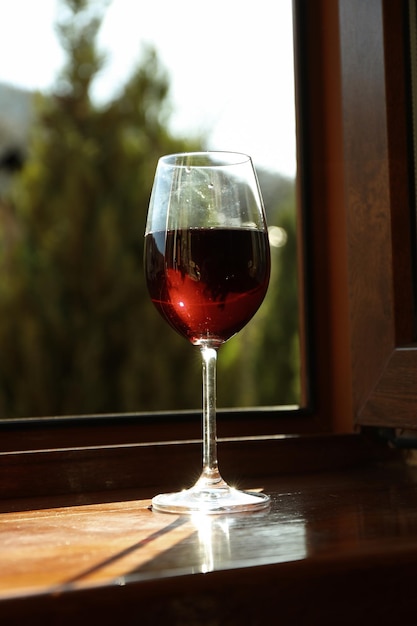 Copa de vino tinto se encuentra en el alféizar de la ventana de madera