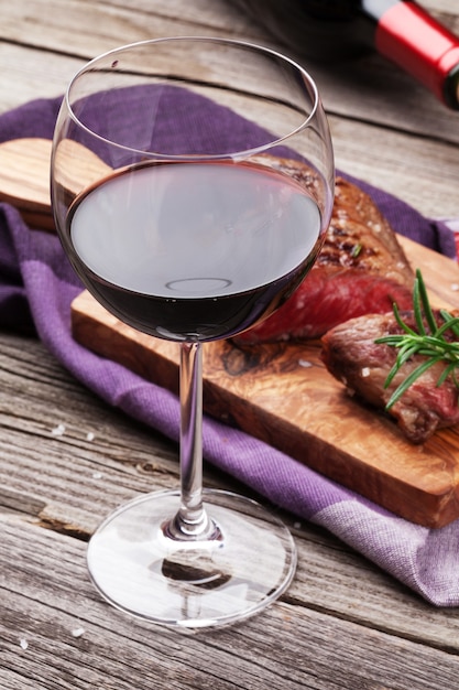 Copa de vino tinto y filete de ternera a la parrilla con romero, sal y pimienta en la mesa de madera