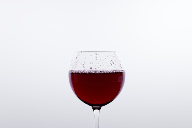 Una copa de vino tinto frente a una pared blanca