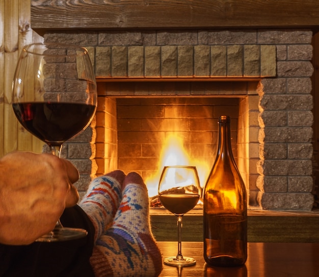 Foto copa de vino tinto en mano de hombre ante acogedora chimenea.