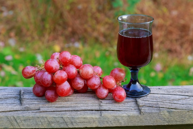 Copa de vino tinto y racimo de uvas en mesa de madera contra viñedo en verano