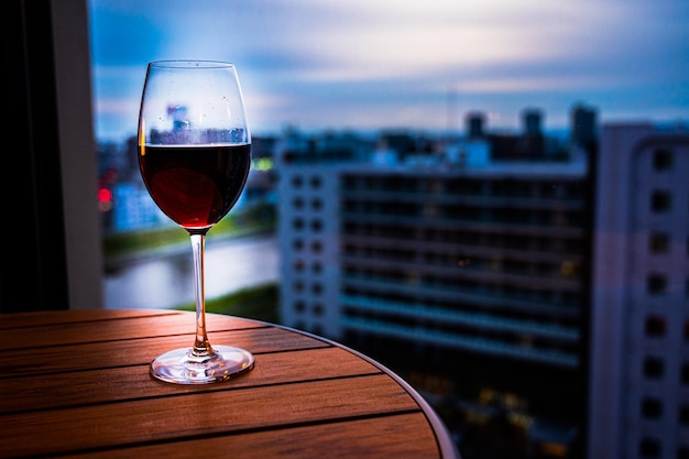 Una copa de vino tinto se sienta en una mesa frente a un paisaje urbano.