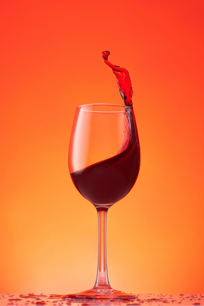 Copa de vino tinto sobre un fondo naranja Salpicaduras de vino tinto en un vaso