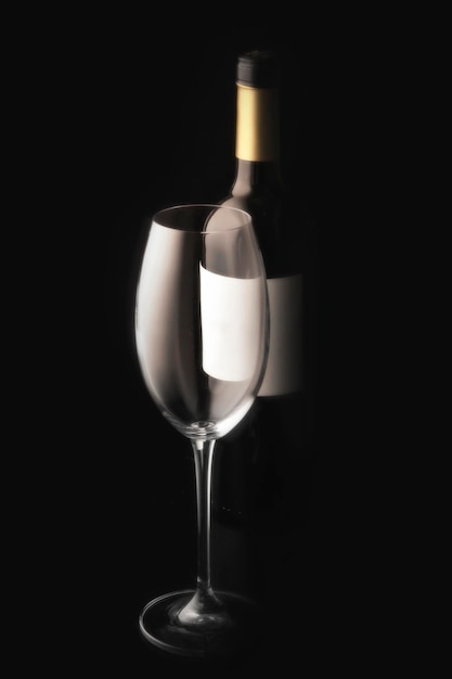 Una copa de vino vacía y una botella de vino tinto sobre un fondo negro con una etiqueta vacía minimalista naturaleza muerta estudio foto vertical