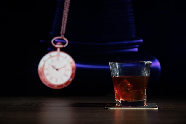 Una copa de whisky en la barra frente al reloj de bolsillo de imagen borrosa