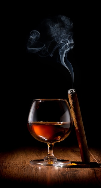 Copa de whisky y cigarro en mesa de madera