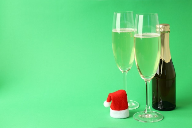 Copas y botella de champán y gorro de Papá Noel sobre fondo verde.