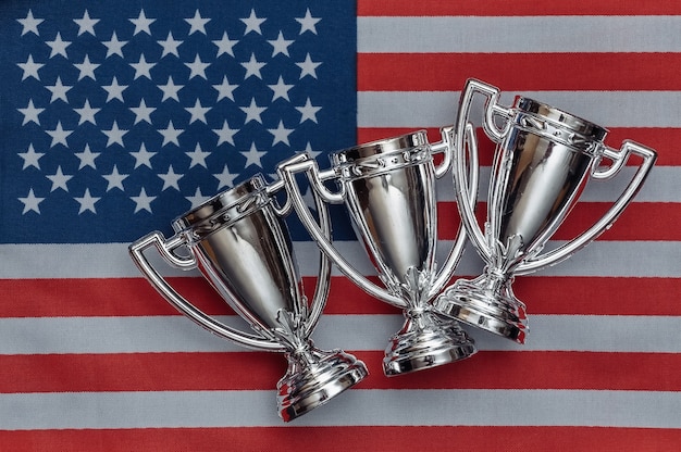 Copas de campeón con pelota de béisbol en la bandera de Estados Unidos. Competiciones deportivas