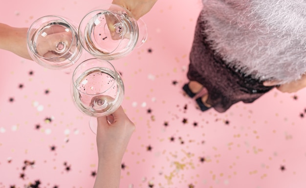 Copas con champagne en manos de las niñas en una fiesta sobre un fondo rosa, copie el espacio.