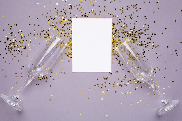 Copas de champán con confeti de estrellas doradas y tarjeta blanca sobre gris