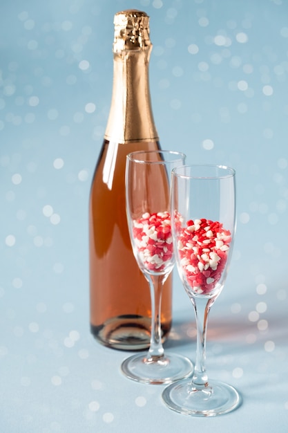 copas de champán con dulces de azúcar en forma de corazón rojo y botella de champán.