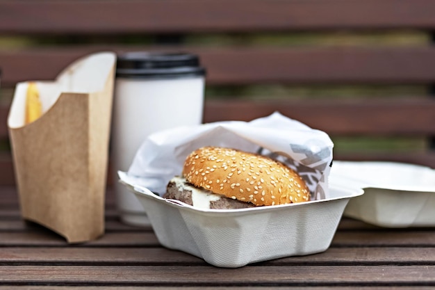 Foto copas de papel de comida rápida con cajas de café hamburguesa y papas fritas en un banco del parque concepto de comida para llevar
