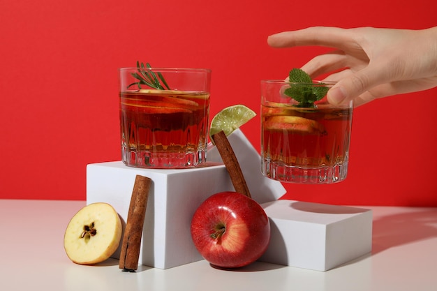 Copas con sidra de manzana, manzanas femeninas y palos de canela sobre un fondo rojo