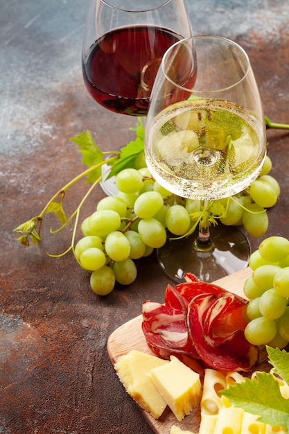 Copas de vino blanco y tinto uva y tabla de aperitivos