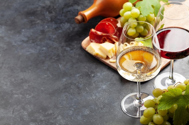 Copas de vino blanco y tinto uva y tabla de aperitivos