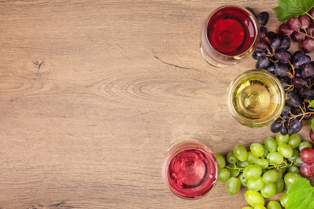 Copas de vino tinto, blanco y rosado y variedad de uva en la vista superior de fondo de madera